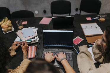 Männlicher Hacker benutzt Laptop inmitten von weiblichen Kollegen im Sitzungssaal eines kreativen Arbeitsplatzes - MASF35551