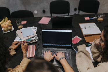 Male hacker using laptop amidst female colleagues in board room at creative workplace - MASF35551