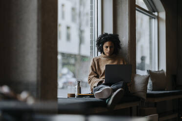 Geschäftsfrau arbeitet am Laptop am Fenster in einem kreativen Büro - MASF35563