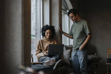 Smiling businesswoman using laptop by male colleague standing in creative office - MASF35565