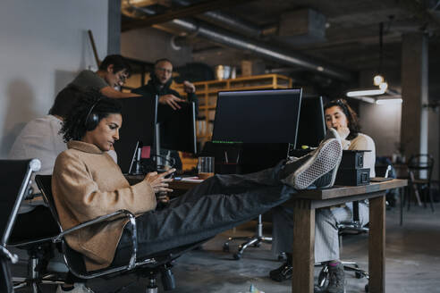 Eine Unternehmerin benutzt ein Smartphone, während ein Computerprogrammierer im Büro arbeitet - MASF35583