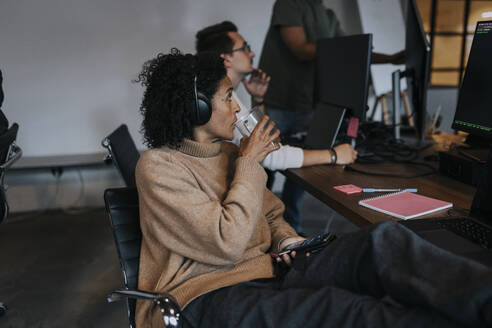 Geschäftsfrau trinkt Kaffee, während sie einen Computerhacker bei der Arbeit in einem Start-up-Unternehmen beobachtet - MASF35584