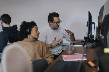 Junger männlicher Programmierer erklärt einer weiblichen Kollegin die Strategie an einem Computer im Büro - MASF35587