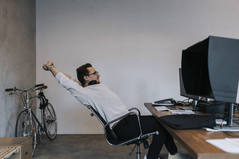 Junger männlicher Hacker, der seine Hände ausstreckt, während er an einem Computer in einem Startup-Unternehmen arbeitet - MASF35590