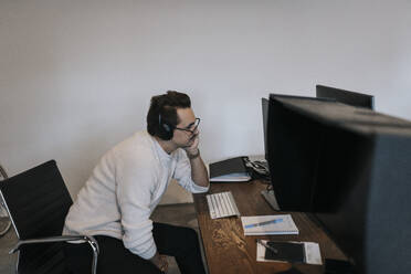 Geschäftsmann mit Hand am Kinn arbeitet über Computer am Schreibtisch in kreativen Büro - MASF35591