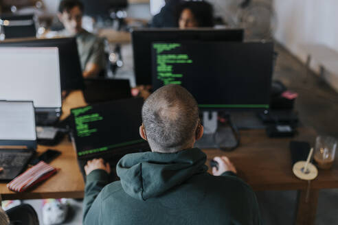 Rear view of male programmer coding on computer at creative office - MASF35593