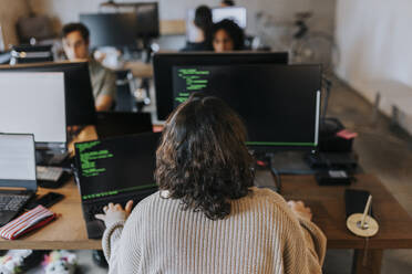 Rückansicht einer jungen Programmiererin, die an einem Schreibtisch im Büro am Computer programmiert - MASF35596