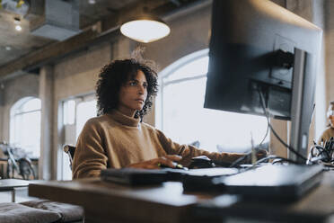 Dedicated female hacker working on computer at desk in startup company - MASF35604