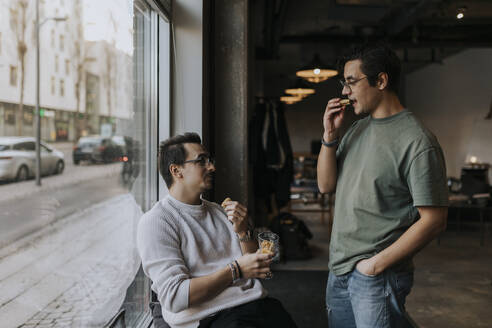 Junge männliche Unternehmer essen in der Pause am kreativen Arbeitsplatz Kekse - MASF35616