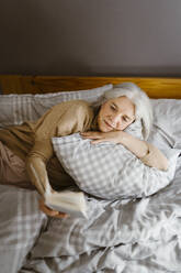 Ältere Frau liest ein Buch, während sie zu Hause auf dem Bett liegt - MASF35633