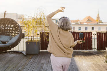 Rückansicht einer älteren Frau, die auf einer Terrasse tanzt und Musik hört - MASF35639