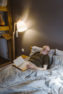 Älterer Mann mit Buch, der ein Nickerchen macht, während er zu Hause auf dem Bett liegt - MASF35660