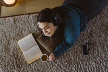 Woman with eyes closed enjoying listening to music while lying on carpet at home - MASF35672