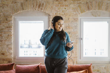 Smiling woman enjoying listening to music through headphones at home - MASF35674