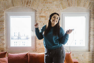 Cheerful woman dancing while listening to music at home - MASF35675