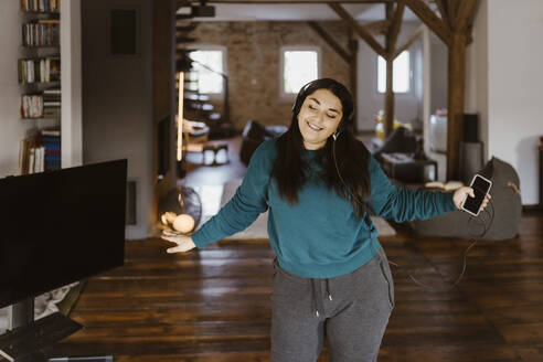 Frau tanzt im Wohnzimmer, während sie zu Hause Musik hört - MASF35677