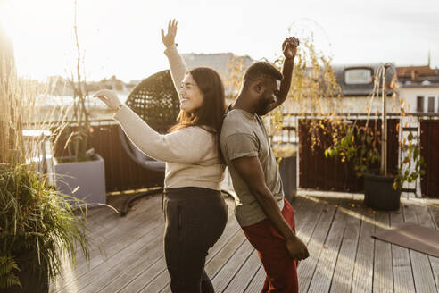 Seitenansicht eines unbekümmerten Paares, das Rücken an Rücken auf einer Terrasse tanzt - MASF35683