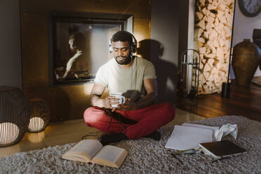 Young man listening to music while reading book at home - MASF35693