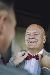Glücklicher glatzköpfiger schwuler Mann sieht seinen Partner an, der vor der Hochzeit seine Fliege zurechtrückt - MASF35704