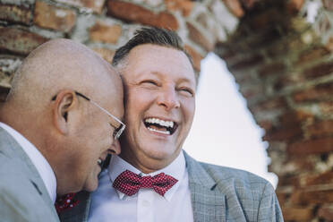 Fröhlicher schwuler Mann lacht mit glatzköpfigem Partner am Hochzeitstag - MASF35711