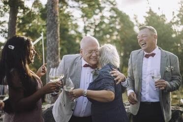 Glatzköpfiger älterer Bräutigam umarmt seine Freundin beim Weintrinken auf der Hochzeitsfeier - MASF35721