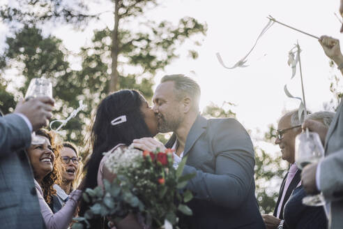 Neuvermähltes Paar küsst sich auf den Mund, während die Gäste ihnen bei der Hochzeitszeremonie zujubeln - MASF35736