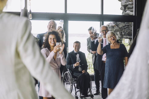 Glückliche multirassische Gäste mit Weingläsern, die dem frisch vermählten Paar bei der Hochzeitszeremonie zujubeln - MASF35738