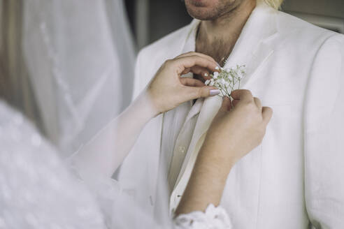 Midsection of bride adjusting boutonniere in groom's pocket on wedding - MASF35741