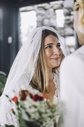 Lächelnde erwachsene Braut im Hochzeitskleid mit Blick auf den Bräutigam - MASF35743