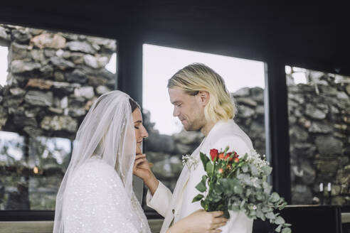 Zärtlicher Bräutigam betrachtet die Braut, die den Brautstrauß hält, am Hochzeitstag - MASF35744