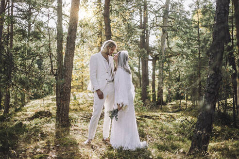Die Braut schaut den Bräutigam an, während sie am Hochzeitstag inmitten von Bäumen im Wald steht - MASF35749