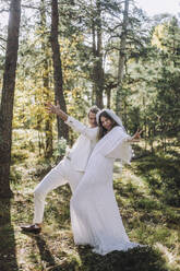 Cheerful newlywed bride and groom gesturing in forest - MASF35755