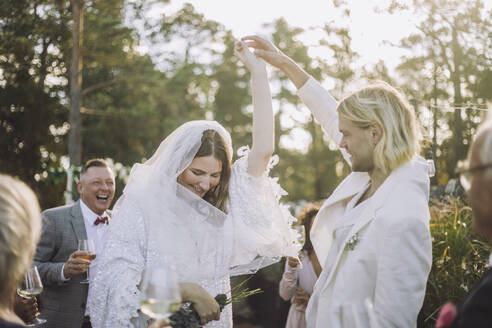 Glücklicher Bräutigam hält die Hand der Braut und tanzt inmitten der Gäste bei einer Hochzeitsfeier - MASF35769