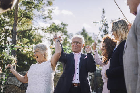 Glückliches Ehepaar hält sich an den Händen und tanzt mit der Familie bei der Hochzeitszeremonie - MASF35783