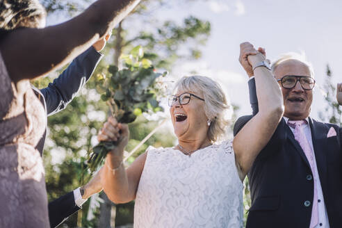 Fröhliches, frisch verheiratetes älteres Paar, das sich an den Händen hält und mit der Familie am Hochzeitstag tanzt - MASF35784