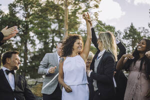 Fröhliches lesbisches Paar tanzt inmitten von Familie und Freunden während einer Hochzeitsfeier - MASF35790