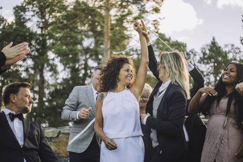 Cheerful lesbian couple dancing amidst family and friends during wedding celebration - MASF35790