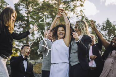 Glückliches lesbisches Paar hält sich an den Händen und tanzt inmitten von Familie und Freunden während der Hochzeitsfeier - MASF35791