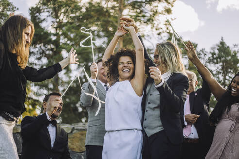 Glückliches lesbisches Paar hält sich an den Händen und tanzt inmitten von Familie und Freunden während der Hochzeitsfeier - MASF35791