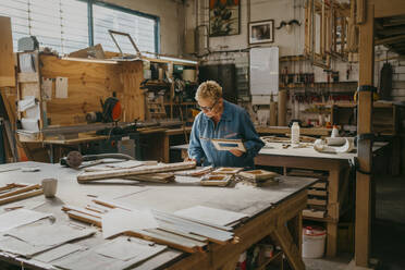 Älterer weiblicher Tischler hält einen Rahmen bei der Arbeit in der Werkstatt - MASF35815