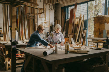 Senior female carpenter assisting colleague while working at repair shop - MASF35824