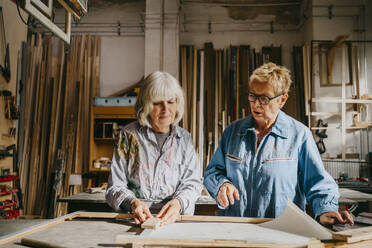 Senior female carpenters discussing with each other while working at workshop - MASF35827