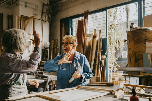 Glückliche ältere Handwerkerinnen beim Abklatschen in der Schreinerei - MASF35828