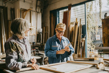 Smiling senior female carpenters talking while working at workshop - MASF35829