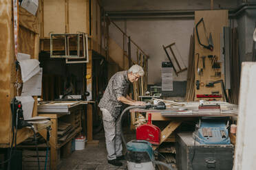 Seitenansicht eines älteren männlichen Schreiners, der in einer Werkstatt stehend an einem Laptop arbeitet - MASF35837