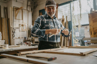 Focused senior male carpenter holding measuring tape at workshop - MASF35841