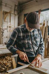Ein älterer Handwerker schabt einen Rahmen mit einem Meißel, während er in einer Schreinerei arbeitet - MASF35842