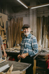 Portrait of smiling senior craftsman standing at workshop - MASF35847