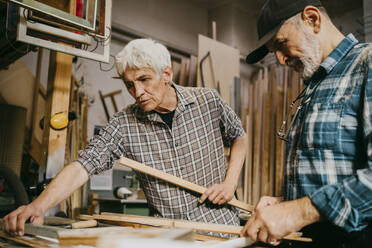 Male carpenter explaining colleague while working together at repair shop - MASF35848