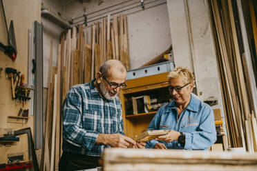 Male and female senior entrepreneurs discussing over frame at repair shop - MASF35849